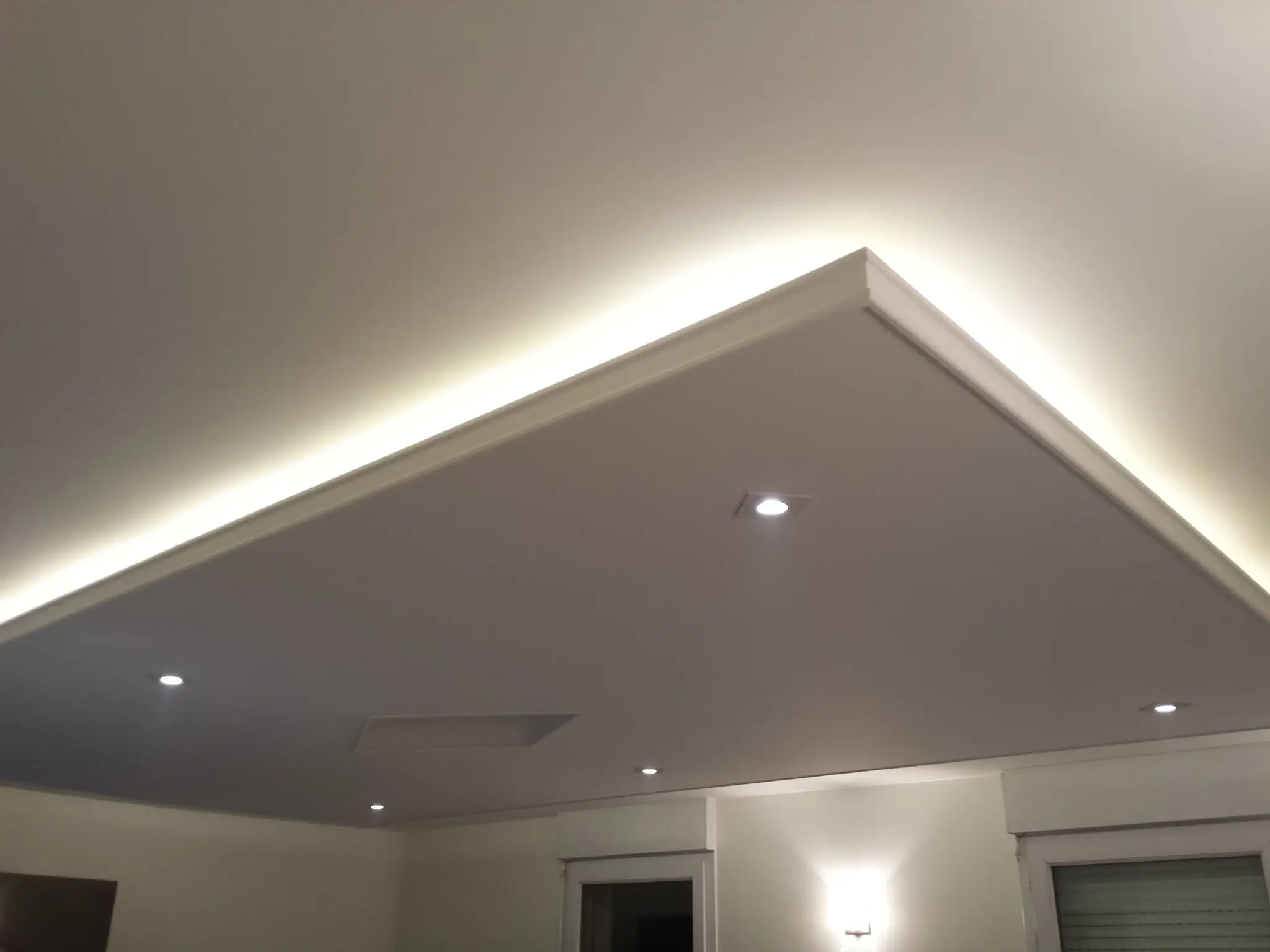 Le faux plafond rectangulaire avec spots encastrés et éclairage indirect périphérique.