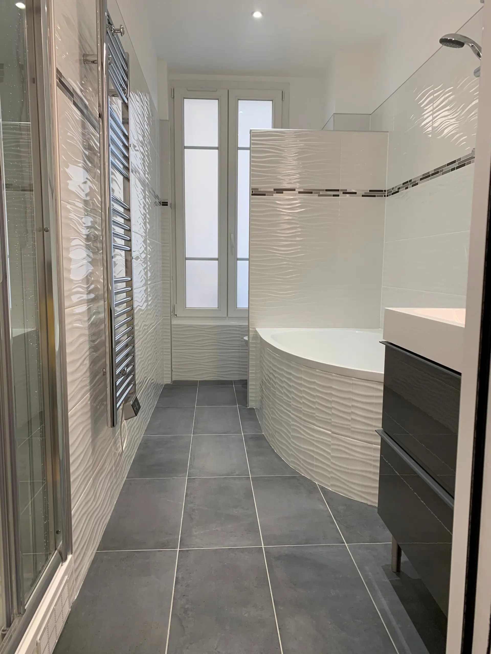 La salle de bain avec paroi courbe carrelée, sèche-serviettes et porte vitrée au fond.