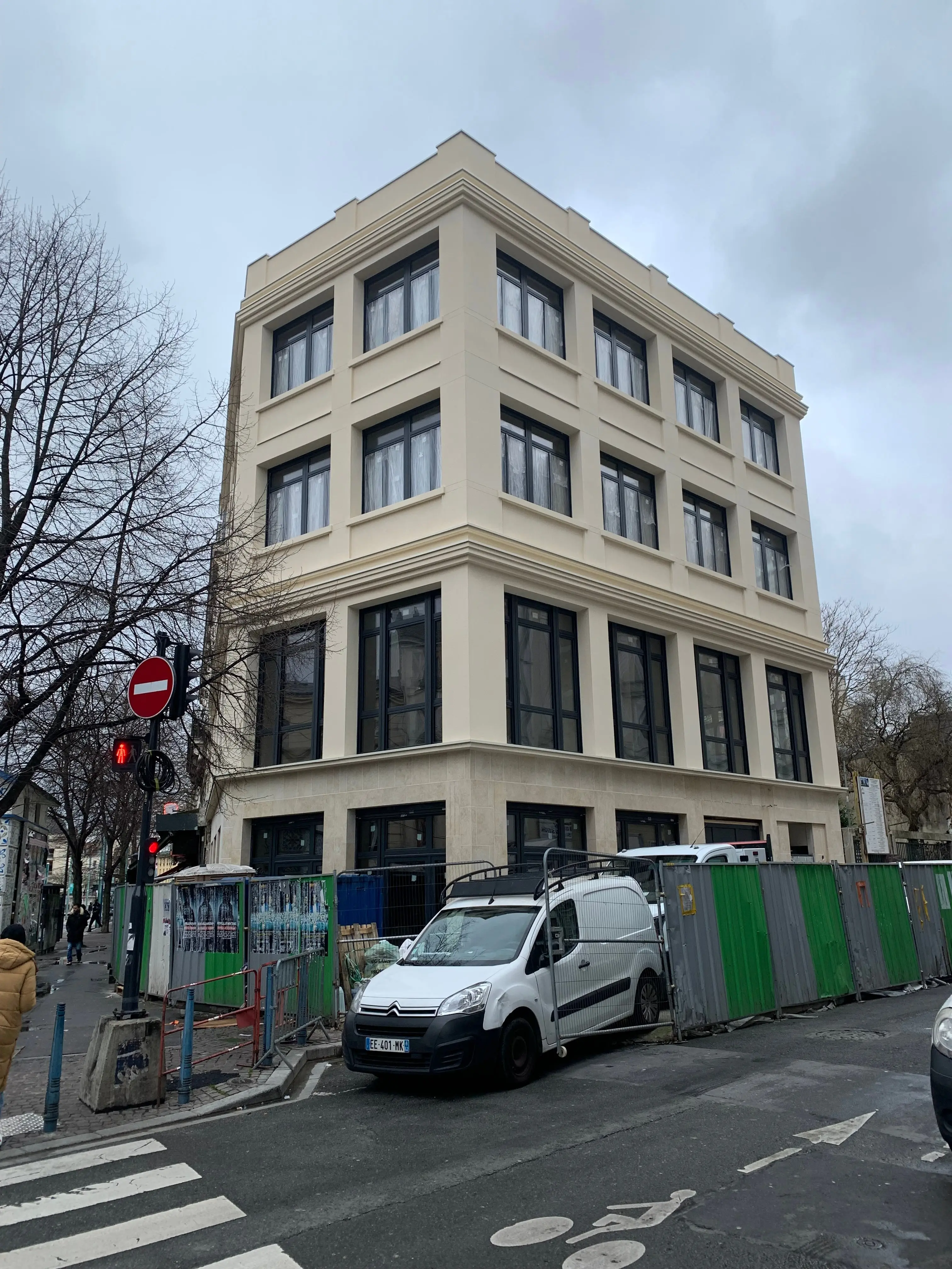 Le bâtiment d’angle à façades claires et fenêtres sombres, derrière une clôture de chantier — chantier à Saint-Denis.